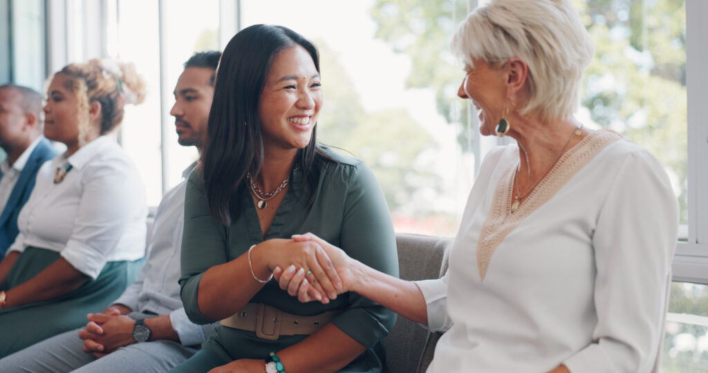 Two women smiling and shaking hands after meeting